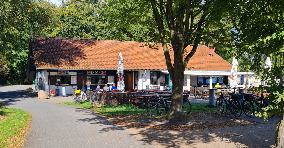 Die Seekate direkt am Strand spiegelt sich im Wasser des Sees. Einige Tretboote liegen am Strand davor.