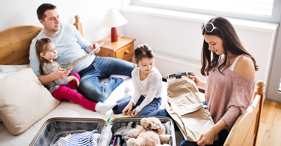 Eine Familie mit Kindern packt auf dem Bett einen Koffer aus